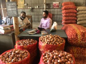 Masud Ahmed sits with colleague at a desk behind bags filled with onions