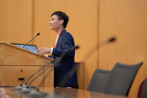 Hai Nguyen. Director of the Unseen Legacies of the Vietnam War Project and Global Vietnam Wars Studies Initiative standing at podium.